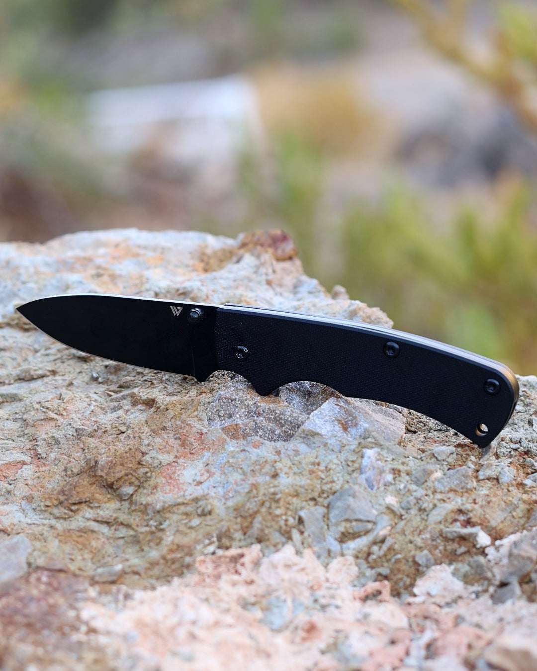 Black folding knife on a rock with a natural background