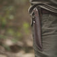 Knife with leather sheath attached to a person's pocket against a blurred natural background