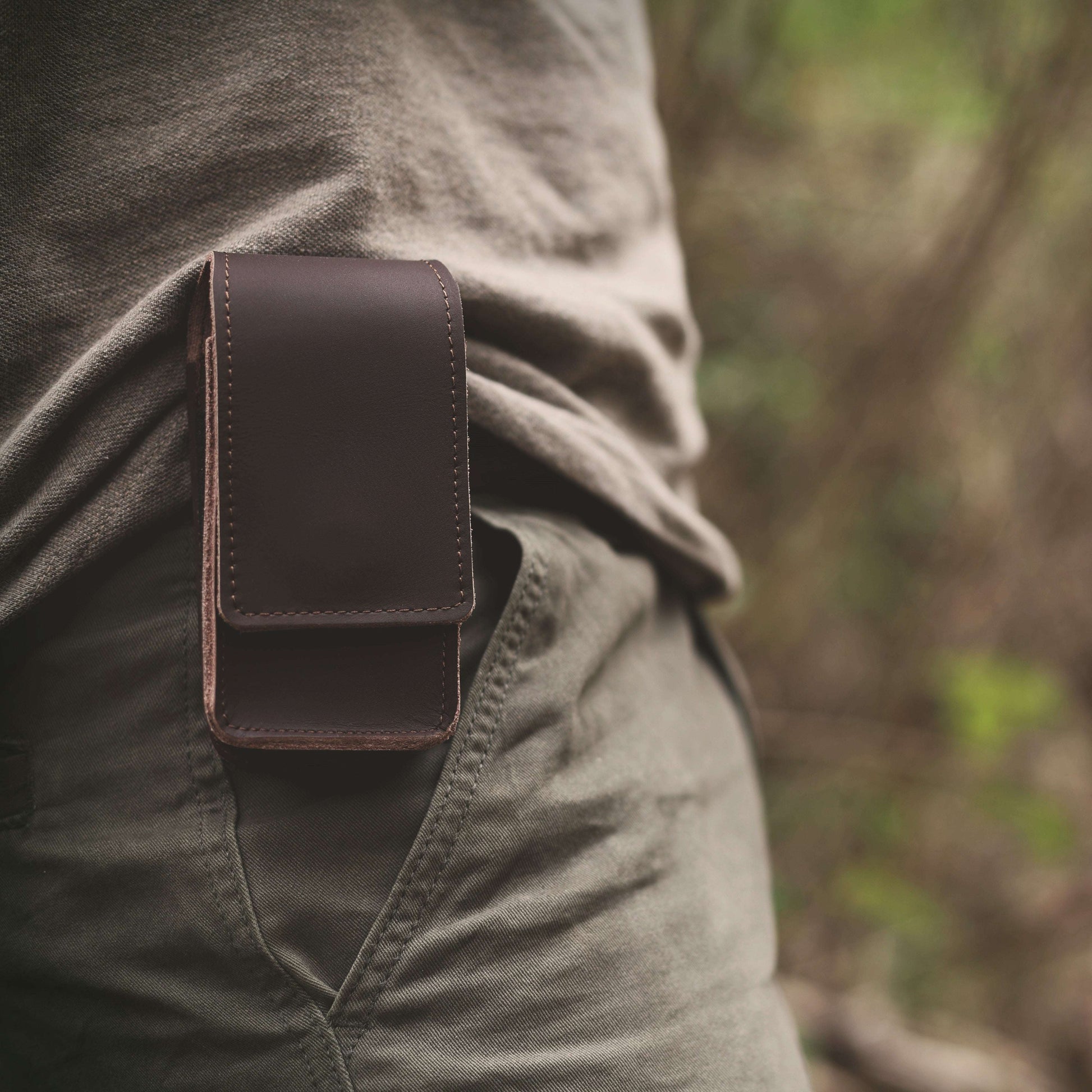 Brown leather pouch attached to a person's green jacket with a blurred natural background