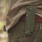Green folding knife attached to a person's pants in a natural setting