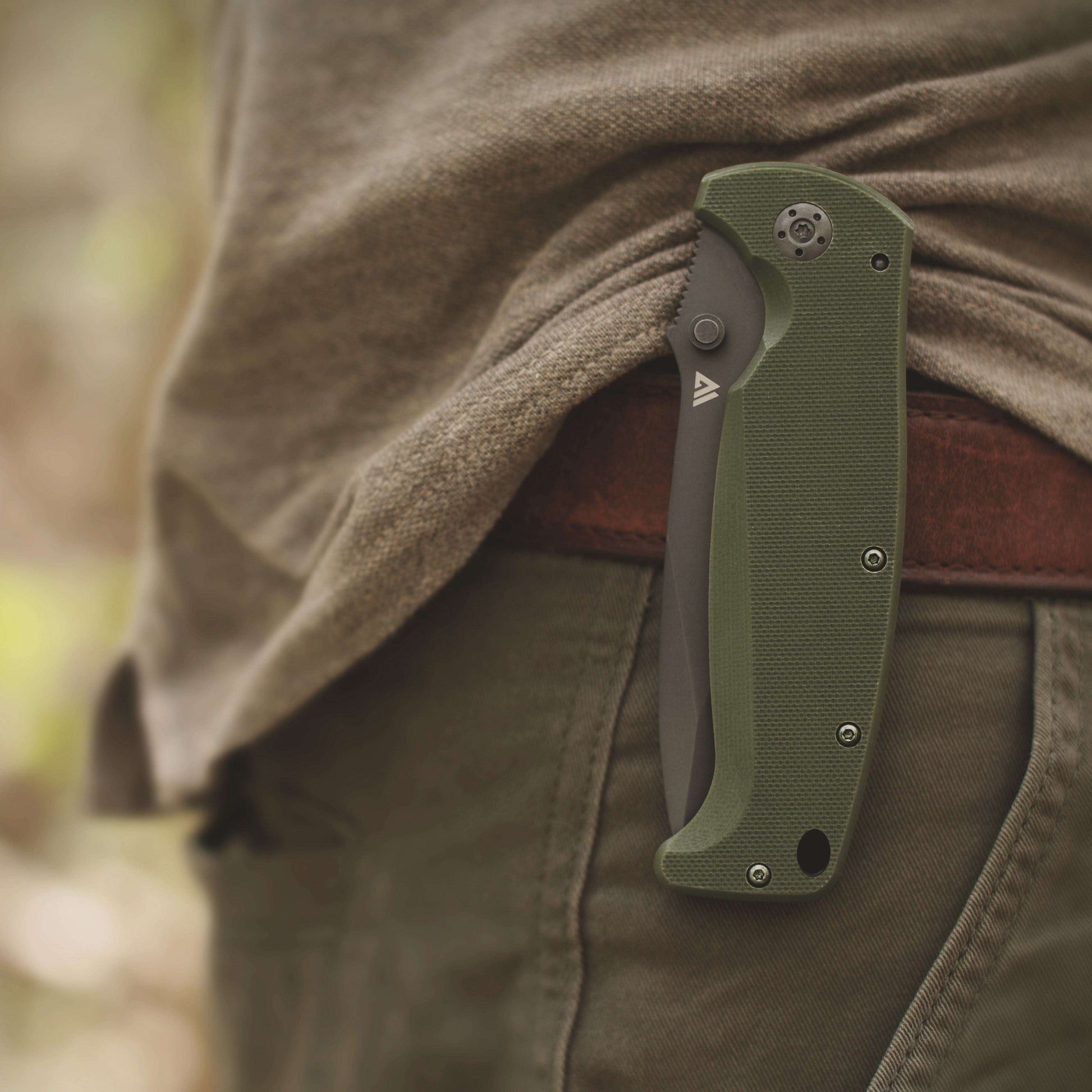 Green folding knife attached to a person's pants in a natural setting