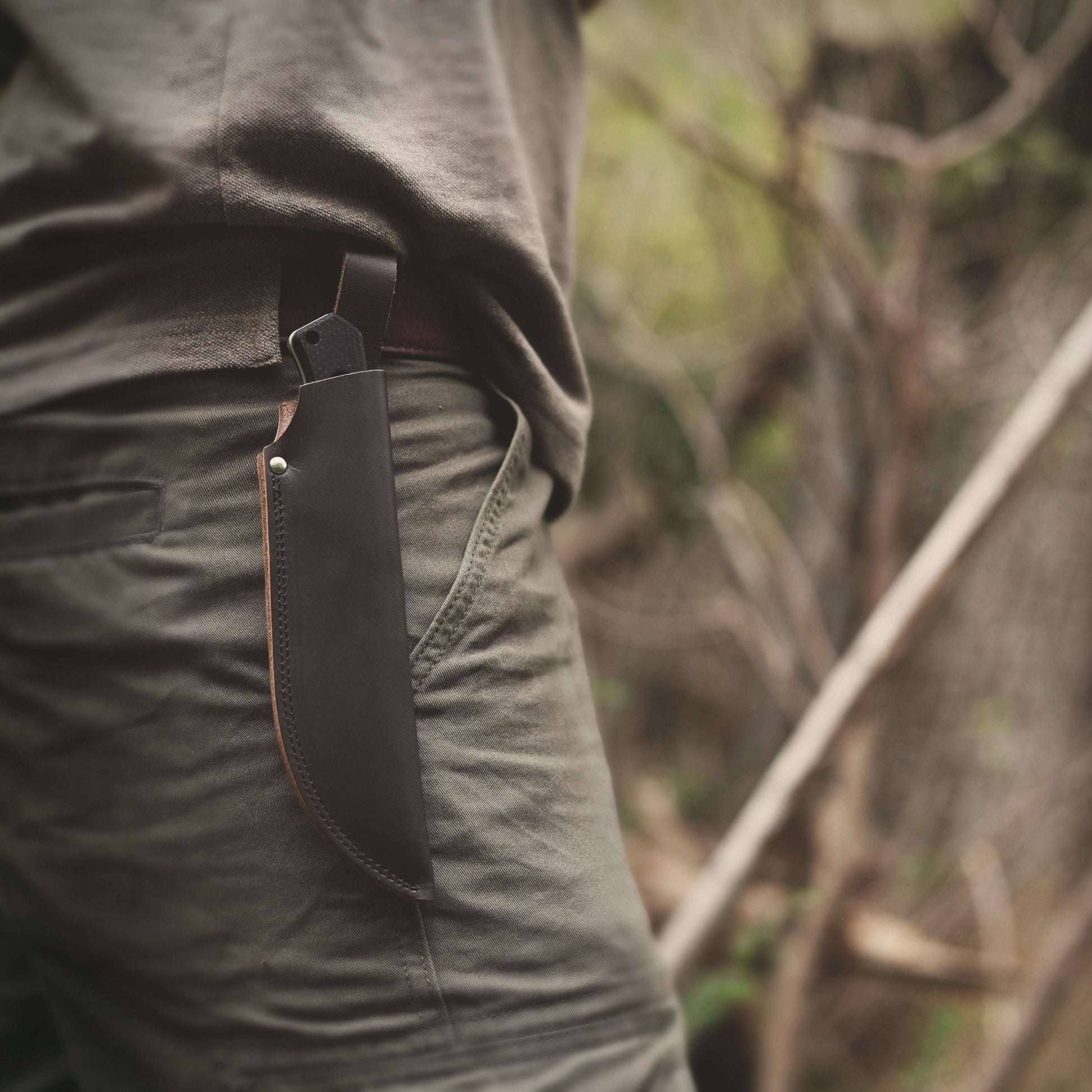 Person wearing a leather knife sheath on a blurred natural background