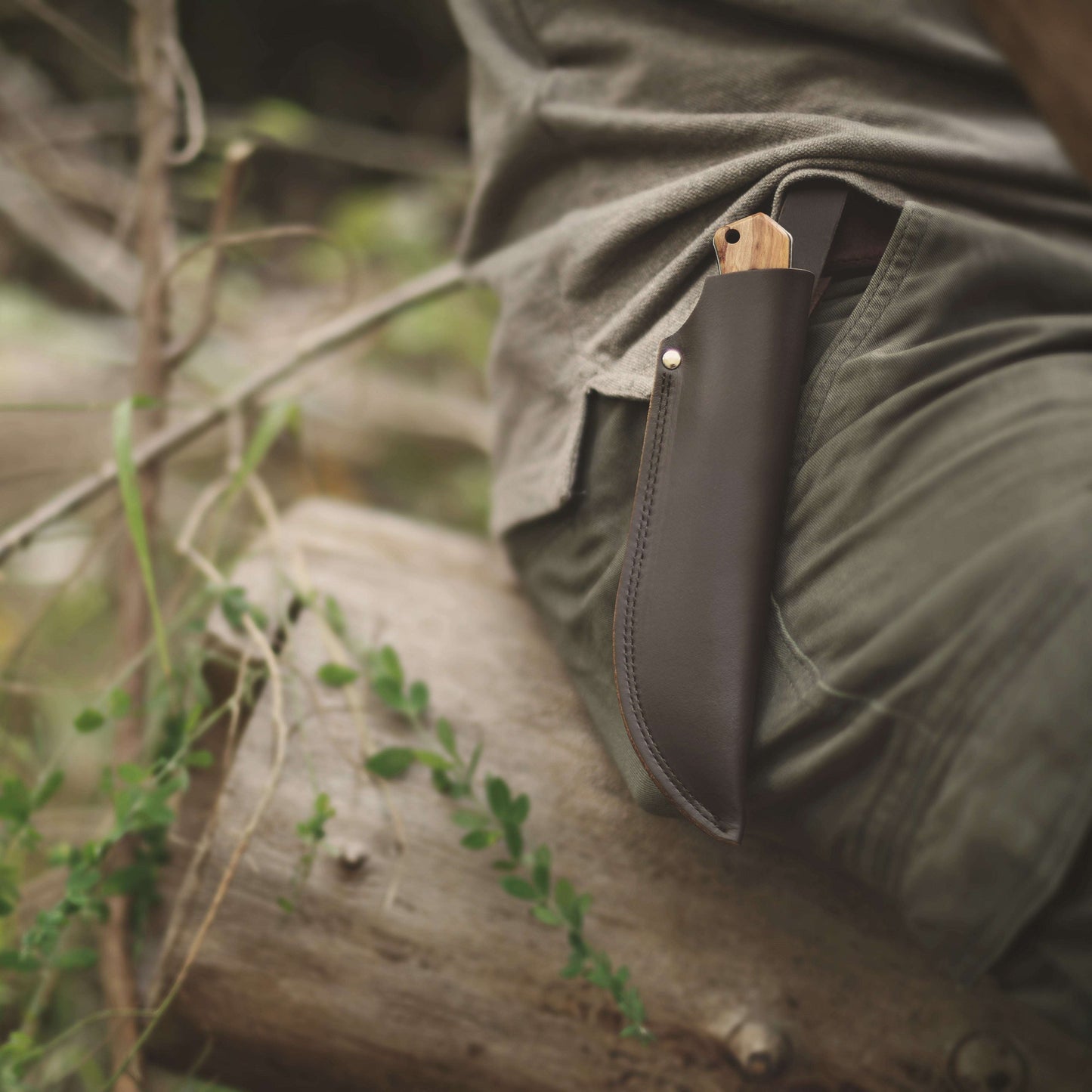 Leather knife sheath on a person's hip with a natural outdoor background