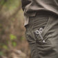Close-up of a person wearing green pants with a zipper detail, blurred natural background