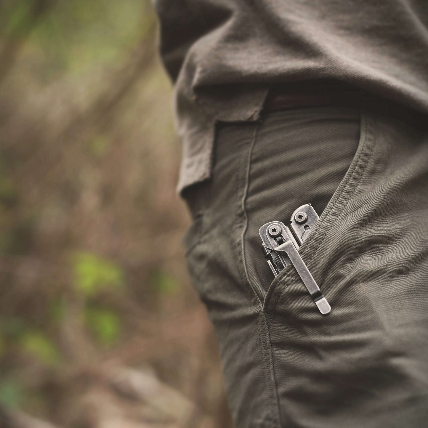 Close-up of a person wearing green pants with a zipper detail, blurred natural background